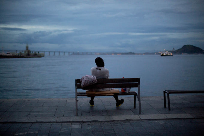   Một người đàn ông vô gia cư ngồi trên ghế sau khi ngủ ở khu vực cảng Rio de Janeiro. Người vô gia cư đang trở thành đối tượng để những người giàu có tấn công.  