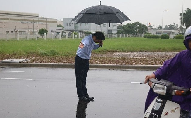 Vị giám đốc người Nhật cúi chào khách hàng đến mua xăng, dầu dưới trời mưa.