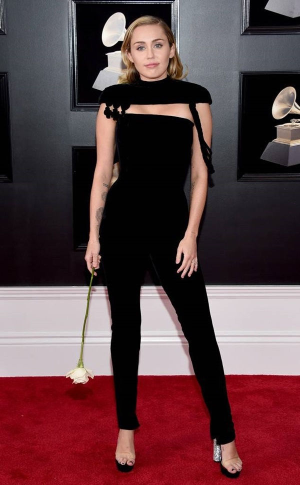 Miley Cyrus cầm theo 1 cành hoa hồng trắng, sải bước tự tin, khoe được thân hình gợi cảm trong bộ đồ đen ôm sát cơ thể.