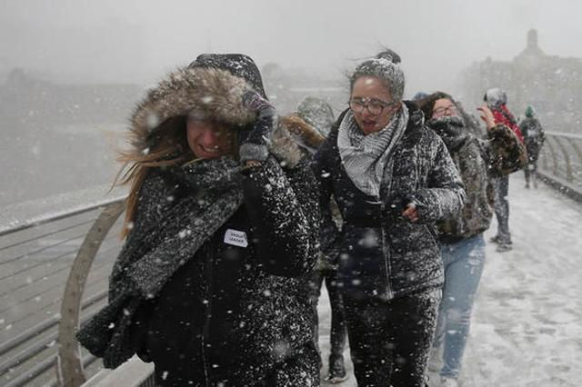 Người dân tại London gặp khó khăn khi đi bộ qua cầu vì gió mạnh và tuyết bám đầy quần áo.