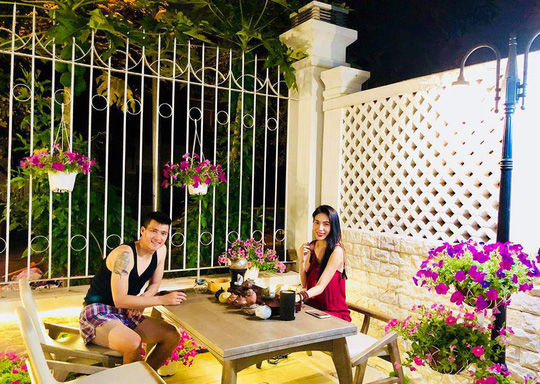 Hình ảnh hai vợ chồng cùng ngồi thư giãn, uống trà trong một góc sân nhà đầy hoa vô cùng lãng mạng.