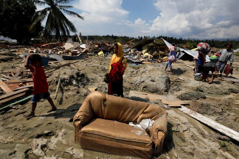   Người dân mang theo đồ đạt đi bộ qua một vũng bùn nơi tàn tích của những ngôi nhà sau khi trận động đất tấn công vào làng Jono Oge ở đảo Sigi, đảo Sulawesi. (Ảnh: Reuters)  