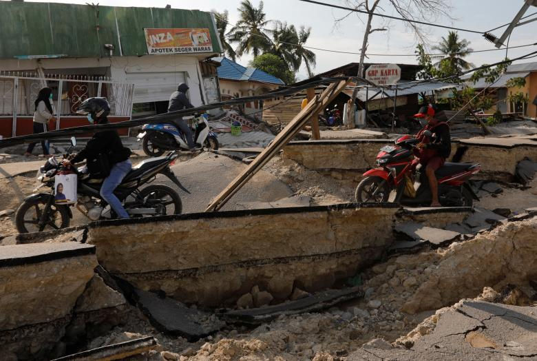   Người dân lái xe gắn máy hai bánh qua một con đường bị hư hại nặng sau khi trận động đất xảy ra. (Ảnh: Reuters)  