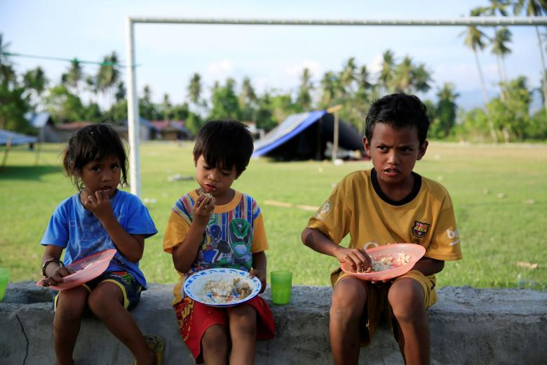   Những đứa trẻ phải ngồi ăn ngoài lều vì lý do an toàn sau trận động đất ở làng Biromaru ở Sigi, đảo Sulawesi. (Ảnh: Reuters)  