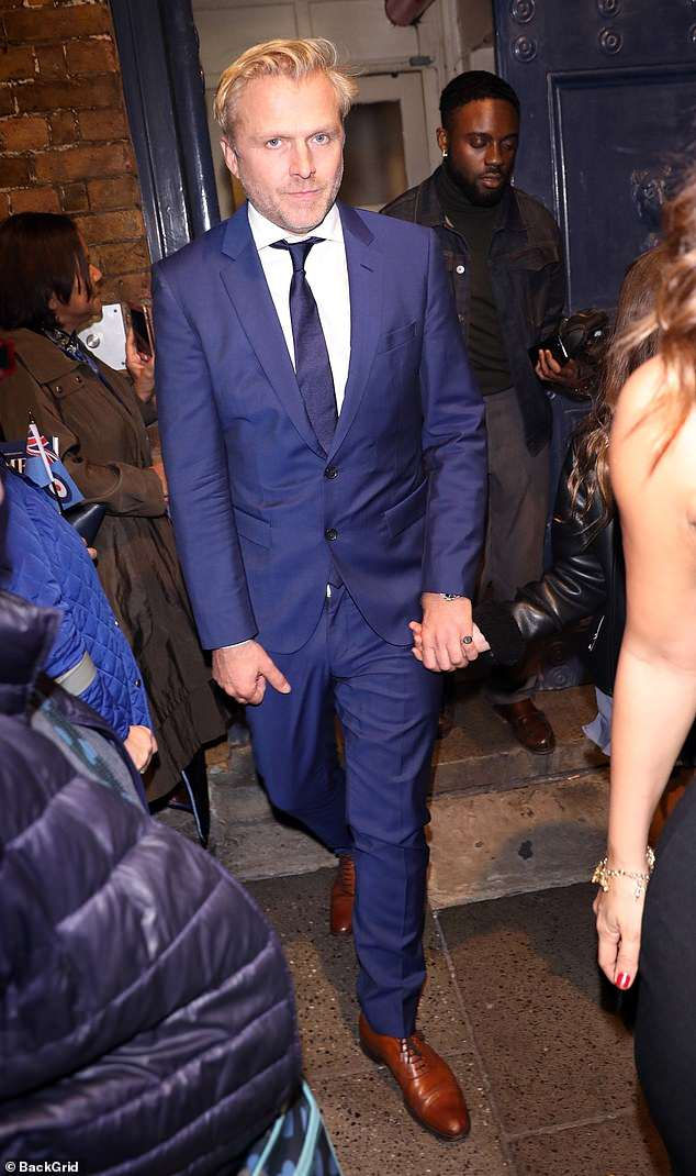 Simon Motson tham dự tiệc tối trong trang phục com lê màu xanh và giày màu nâu mạnh mẽ.