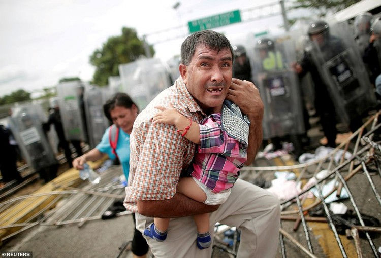 Một người di cư gốc Trinidad bảo vệ con của anh sau khi những người di cư khác tìm cách tới Mỹ đã xông vào một trạm kiểm soát biên giới ở Guatemala, thành phố Ciudad Hidalgo, Mexico. (Ảnh chụp ngày 19/10/2018 bởi nhiếp ảnh gia Ueslei Marcelino).