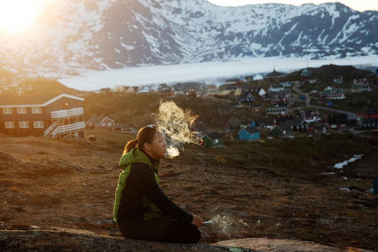 Một cô gái trẻ ngồi trên một hòn đá và hút thuốc.