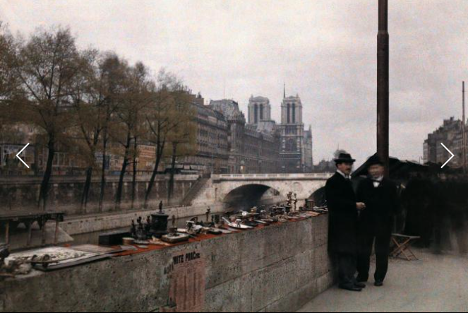Hai người đàn ông đứng cạnh đồ trang sức để bán trên bờ sông Seine vào những năm 1920, Nhà thờ Đức Bà ở phía sau đó.