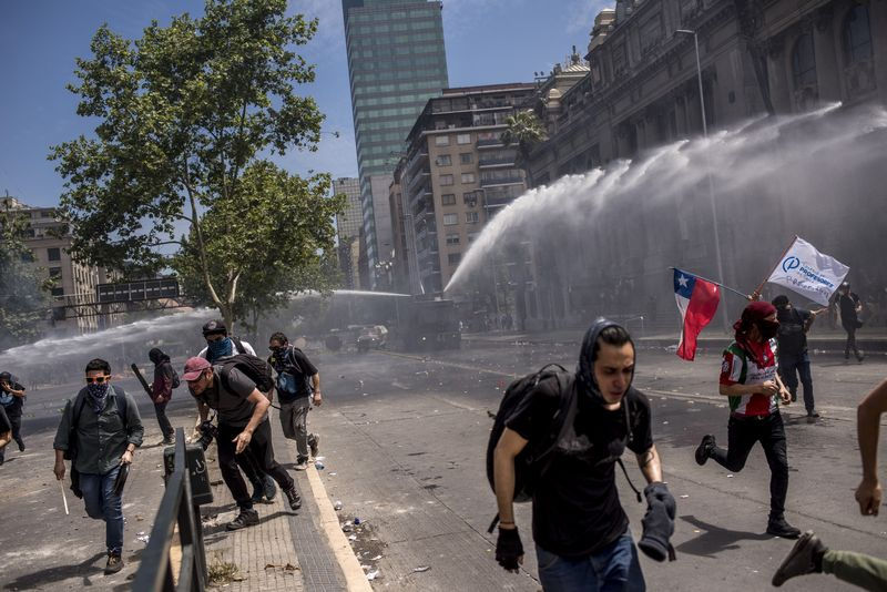 Người biểu tình bỏ chảy dưới vòi rồng của cảnh sát chống bạo động trong một cuộc biểu tình ở Santiago, Chile vào ngày 23/10. Ảnh: Cristobal Olivares/Bloomberg.