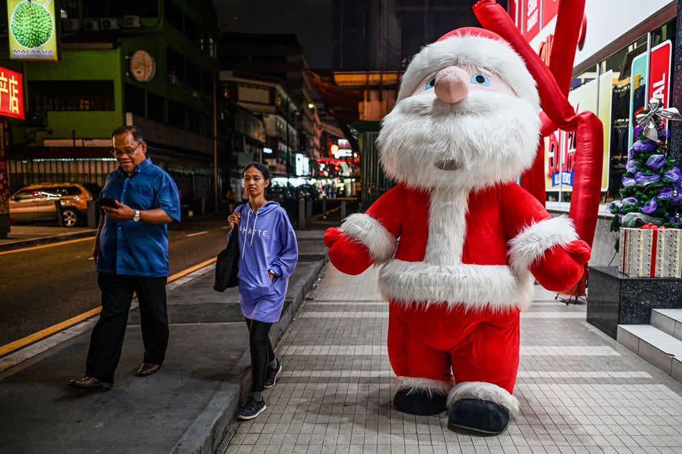 Người đi bộ đi ngang qua một người đàn ông mặc trang phục ông già Noel khổng lồ bên ngoài một trung tâm mua sắm ở Kuala Lumpur vào ngày 11/12. Ảnh: AFP / Getty. 