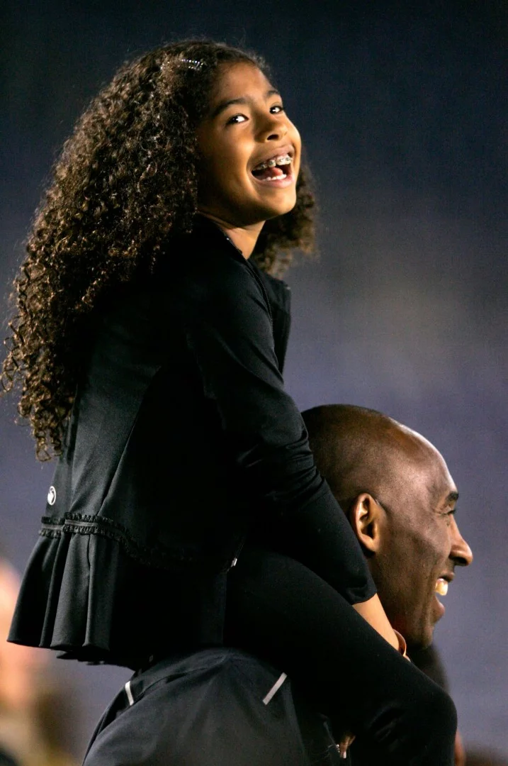 Bức ảnh này được chụp vào năm 2014 tại CLB Los Angeles Lakers, Kobe Bryant đứng bên lề với cô con gái Gianna Maria-Onore Bryant trên vai trước khi bắt đầu trận đấu với Mỹ và Trung Quốc tại SVĐ Qualcomm ở TP. San Diego, bang California. Ảnh: AFP.