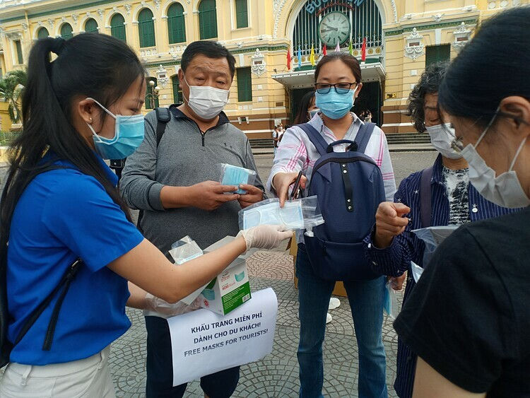 Tình nguyện viên phát miễn phí khẩu trang cho nhóm khách quốc tế trước Bưu điện Thành phố. Ảnh: Nguyễn Nam.