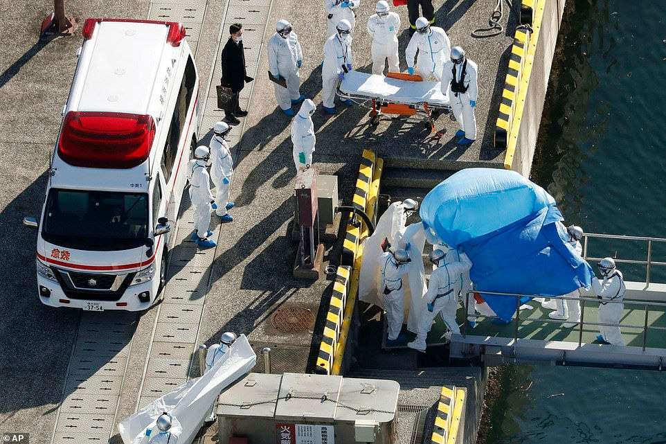 Nhân viên y tế trong bộ đồ bảo hộ dẫn một hành khách được xét nghiệm dương tính với một loại coronavirus mới từ tàu du lịch Diamond Princess tại cảng Yokohama. Ảnh: AP.