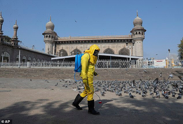   Một nhân viên y tế mặc một bộ đồ bảo hộ màu vàng thực hiện công việc khử trùng bên ngoài một nhà thờ Hồi giáo ở thành phố Hyderabad, Ấn Độ.  