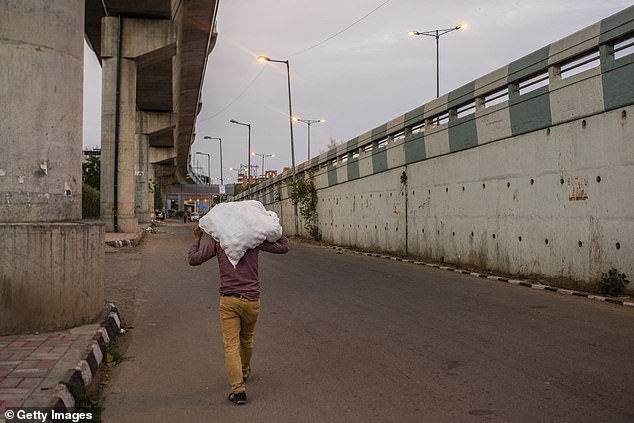   Một người đàn ông Ấn Độ mang túi trên vai khi anh ta đi trên một con đường vắng ở New Delhi hôm nay (24/3).  