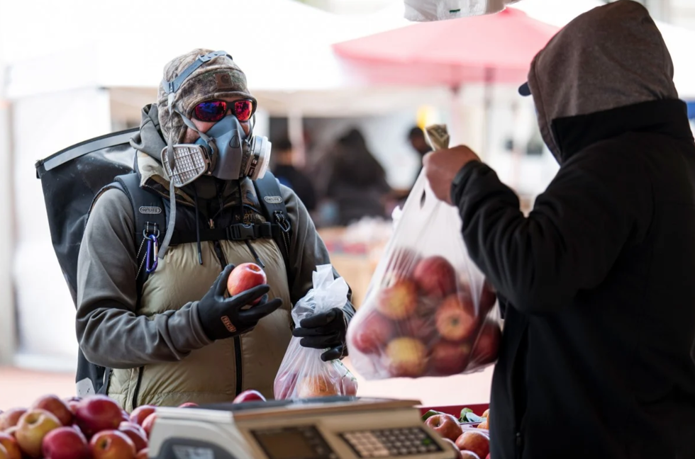   Một khách hàng đeo mặt nạ bảo hộ và găng tay, rời đi, mua táo tại chợ nông sản ở San Francisco vào thứ Tư. Ảnh: Bloomberg  