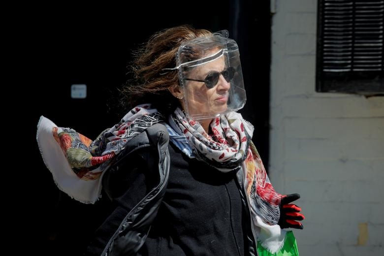   Một người phụ nữ đeo mặt nạ chống giọt bắn bằng nhựa để bảo vệ trong khi dịch COVID-19 bùng phát ở Brooklyn, thành phố New York (ảnh trái) và Mọi người đi bộ ở Quảng trường Thời đại, Manhattan, phía trên là một số màn hình được chiếu sáng màu xanh lam như một phần của sáng kiến ​​
