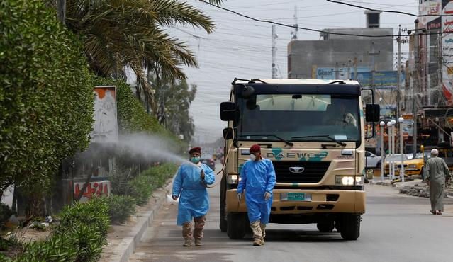 Quân đội Iraq mặc một bộ đồ bảo vệ phun thuốc khử trùng để vệ sinh đường phố, trong giờ giới nghiêm. Ảnh: REUTERS.