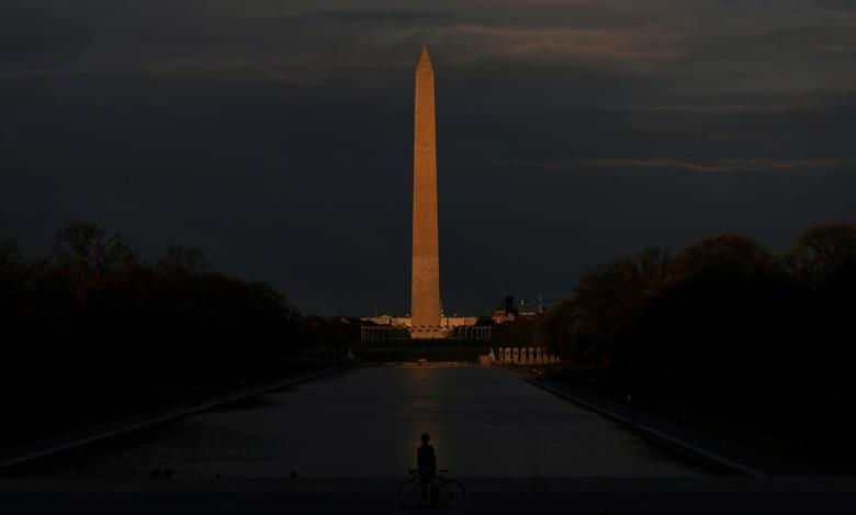     Một người đi xe đạp dừng trước Hồ bơi phản chiếu Lincoln Tưởng niệm, với Đài tưởng niệm Washington được thắp sáng bởi mặt trời lặn ở phía sau, tại Washington. 
