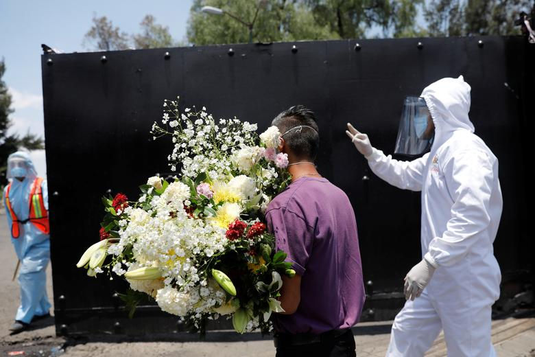 Một người đàn ông với hoa trong tay khi các công nhân thành phố bảo vệ lối vào nghĩa trang do thông báo của chính phủ sẽ đóng cửa vào cuối tuần.