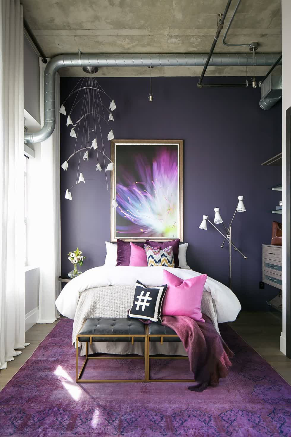 Trần bê tông và ống dẫn tiếp xúc mang lại vẻ đẹp công nghiệp cho phòng ngủ đầy màu sắc này trong căn phòng màu tím này.