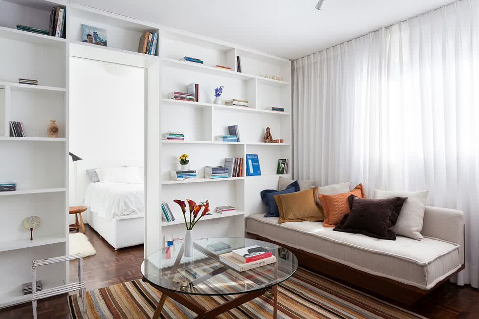 Trước tiên là thiết kế phòng khách của căn hộ 30m2 được bài trí tối giản với ghế sofa mô-đun đặt cạnh cửa sổ kính lớn, kế đến là kệ sách rộng rãi trong khu vực sinh hoạt cùng với tấm thảm sọc đầy màu sắc.