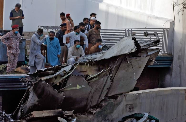   Mọi người đứng cạnh mảnh vỡ của một chiếc máy bay sau khi bị rơi ở khu dân cư gần sân bay ở thành phố Karachi, Pakistan.  