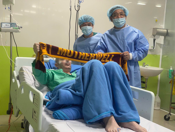 Ông Lương Ngọc Khuê (bên phải) và bệnh nhân 91 cùng nâng món quà được gửi từ quê hương: chiếc khăn có ghi tên đội bóng mà anh yêu thích. Ảnh: Tuổi Trẻ 