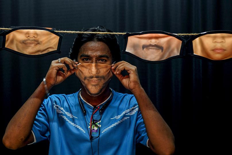Một người đàn ông điều chỉnh khẩu trang với hình ảnh khuôn mặt được in trên đó khi các khẩu trang khác được treo phía sau. Ảnh chụp tại Chennai, Ấn Độ. Ảnh: AFP.