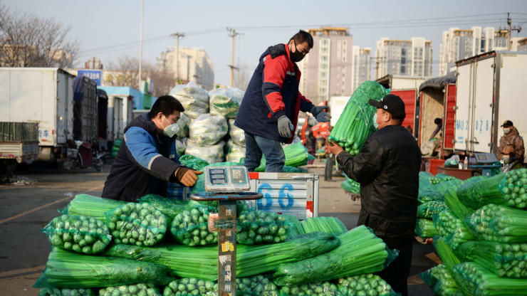   Những người đeo khẩu trang di chuyển các gói rau tại một chợ bán buôn các sản phẩm nông nghiệp tại Bắc Kinh, Trung Quốc. Ảnh: Reuters.  