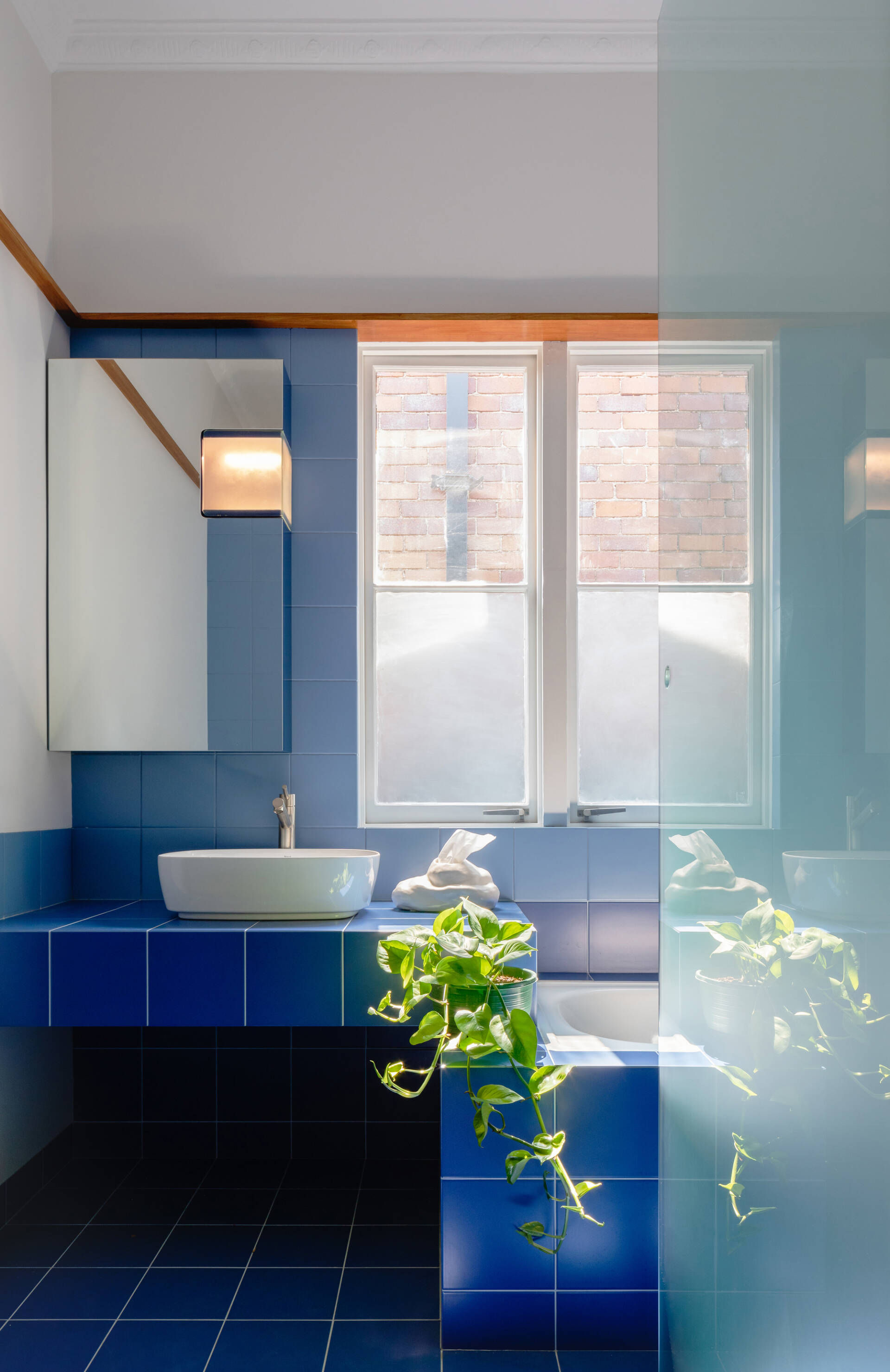 Phòng tắm được cải tạo từ phòng ngủ thứ hai với tường và sàn ốp lát gạch men màu xanh coban cùng tông với cầu thang, sàn tầng 2, tủ bếp, khung cửa mặt tiền.