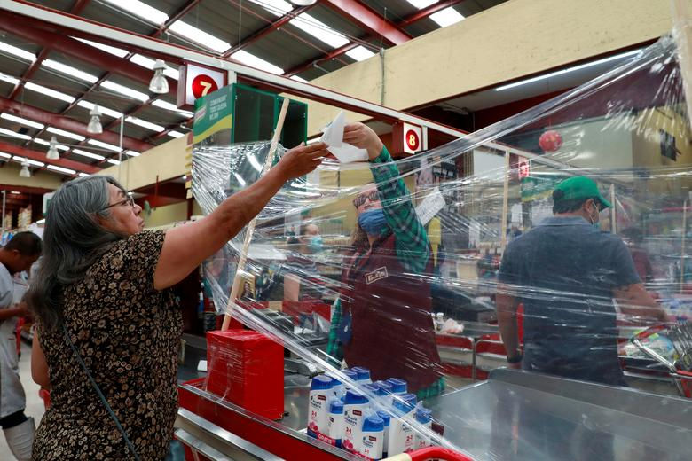 Một nhân viên thu ngân phục vụ khách hàng sau hàng rào nhựa dựng tạm tại siêu thị Garis ở Toluca, Mexico. Ảnh: Reuters.