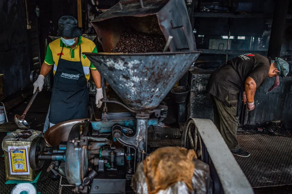   Một công nhân (bên trái) đổ cà phê pha đương vào chiếc hôp thiết để bán tại xưởng cà phê Antong ở Taiping, Malaysia. Ảnh: AFP.  