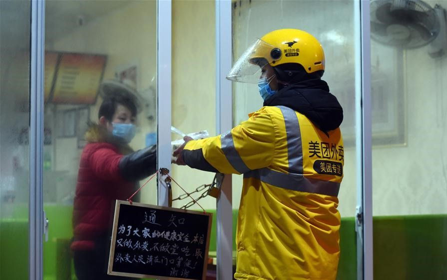 Một nhân viên giao hàng của Meituan cẩn thận đưa thức ăn qua những cánh cửa bị xích vì cách ly trong đại dịch.Ảnh: Xinhua
