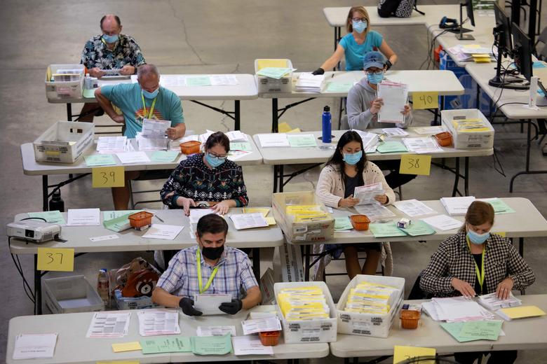 Nhân viên bầu cử sắp xếp thông qua một số trong số hàng ngàn lá phiếu gửi qua thư tại Cơ quan Đăng ký Cử tri quận Cam ở Santa Ana, California, (ảnh trái) và một thành viên của ban kiểm duyệt Hạt Pinellas xử lý các lá phiếu vào ngày bầu cử ở Largo, Florida, (ảnh phải). Ảnh: Reuters