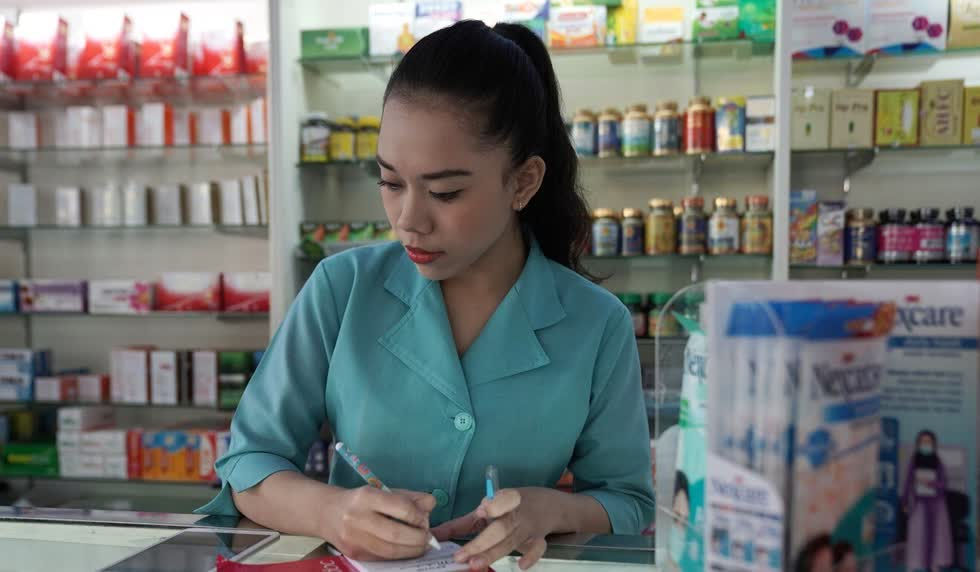 Một nhân viên viết trên tập giấy kê đơn khi đang xem nền tảng chăm sóc sức khỏe trực tuyến của Halodoc trên điện thoại thông minh tại một hiệu thuốc Apotik Mahakam ở Jakarta, Indonesia, vào ngày 11/7/2019. Có khoảng 40 triệu người kết nối với ứng dụng hoặc trang web của Halodoc liên kết người dùng với hơn 20.000 bác sĩ được cấp phép ở Indonesia để được tư vấn trực tuyến. Sau khi được chẩn đoán, bệnh nhân có thể mua thuốc thông qua ứng dụng từ một trong hơn 1.500 hiệu thuốc và được giao thuốc trong vòng vài phút bằng xe máy thông qua Gojek. Ảnh: Bloomberg