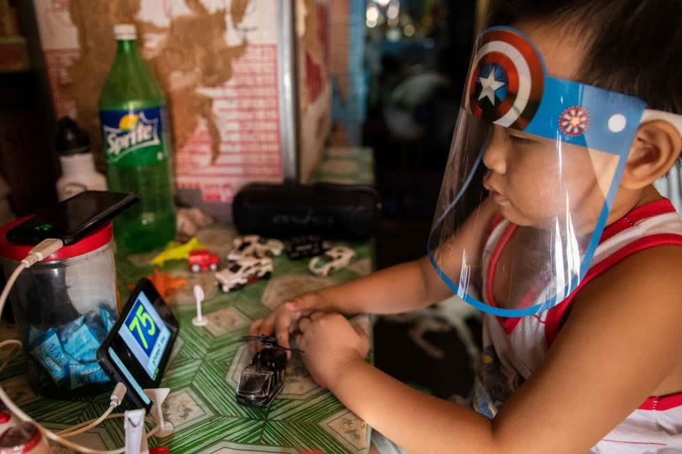   Một cậu bé đeo tấm che mặt khi xem chương trình học trực tuyến trên điện thoại thông minh ở Manila, Philippines, ngày 17/8. Ảnh: Reuters  