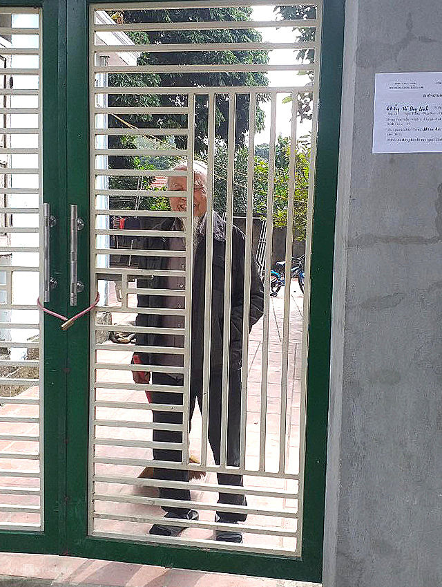 Một cụ ông ở thôn Xa Liễn đứng trong căn nhà của gia đình bị cách ly. Trước cổng, chính quyền dán thông báo để tránh người dân tiếp xúc gần. Ảnh: Lam Sơn.