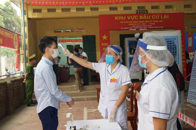 Lực lượng y tế kiểm tra thân nhiệt một cử tri tại điểm bỏ phiếu ở xã Tráng Việt, Mê Linh. Ảnh: Phạm Hùng.