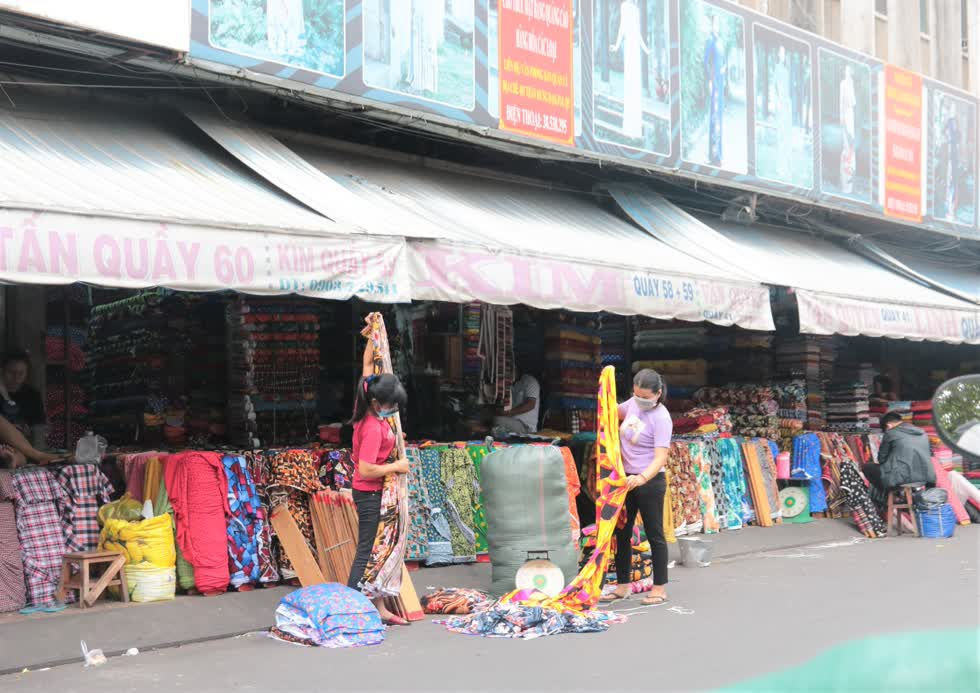 Phía trước khu chợ, tận dụng mặt đường, một số chị em tiểu thương bày vải ra để đo, cắt, sắp xếp thành từng sấp vải gọn gàng trong cửa tiệm.