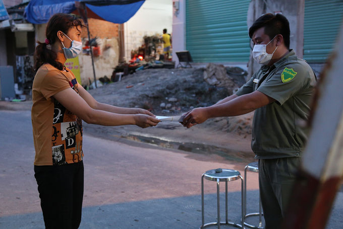 Người dân (trái) phường Thạnh Lộc, quận 12, được phát phiếu hỗ trợ mua đồ dùng, chiều 30/5. Ảnh: Đình Văn.
