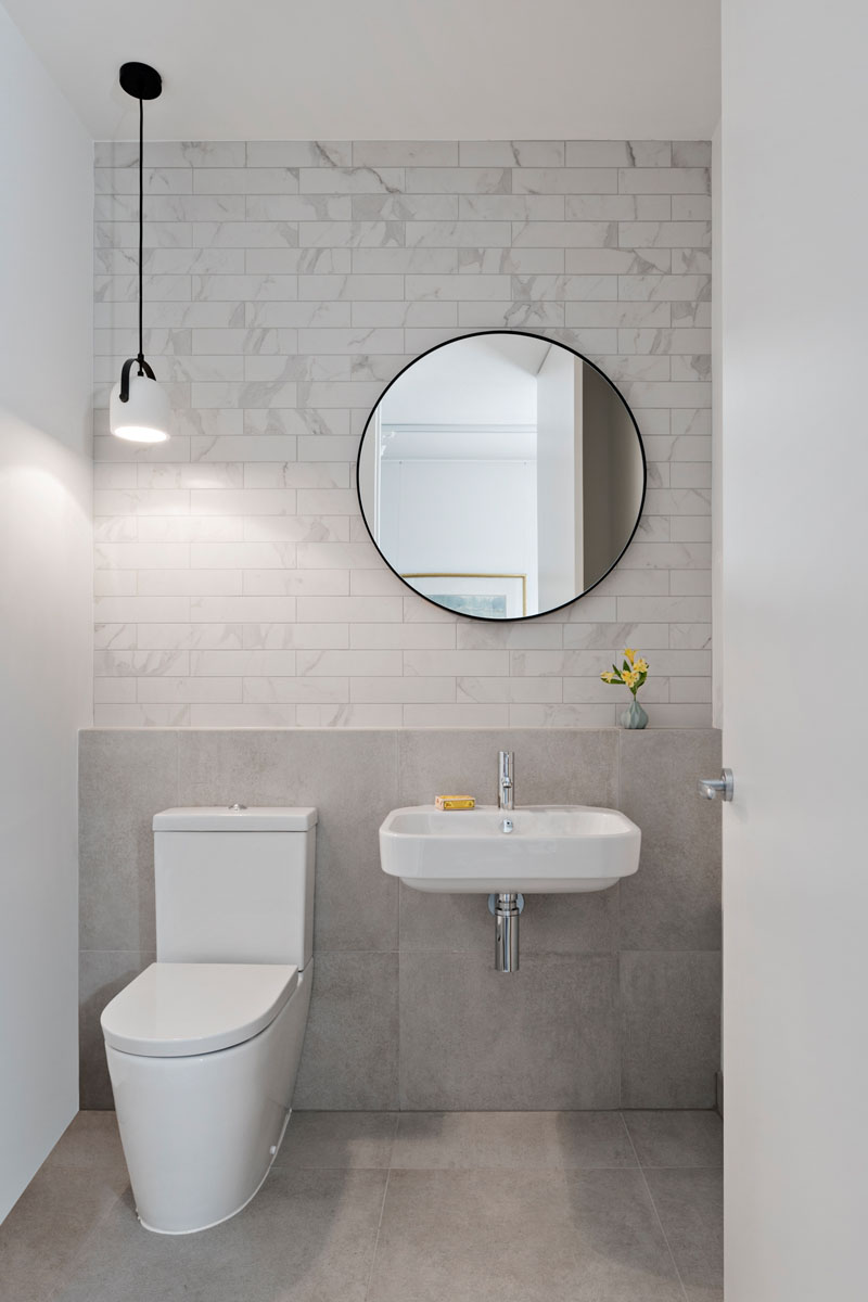 Phòng tắm tối giản này bao gồm gạch trắng và xám nhạt lát tường phía sau, trong khi một đèn mặt dây trắng và đen treo phía trên nhà vệ sinh.